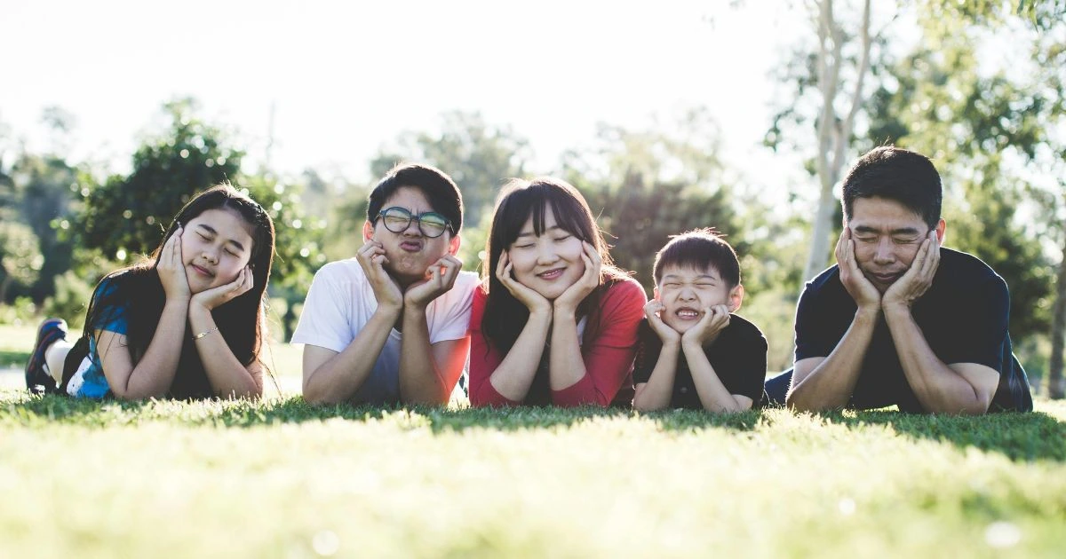 Mindfulness and Parenting , A happy family of five lying on the grass outdoors, resting their faces on their hands in a playful and relaxed manner, enjoying a mindful moment together in nature.
