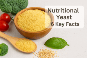 What Is Nutritional Yeast? A bowl and wooden spoon filled with golden nutritional yeast flakes surrounded by fresh vegetables, illustrating what nutritional yeast is.